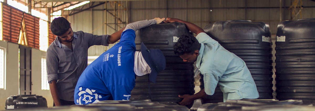 Un voluntario CADENA y un ciudadano Indio ayudan a cargar un tanque de agua en la misión a Kerala.