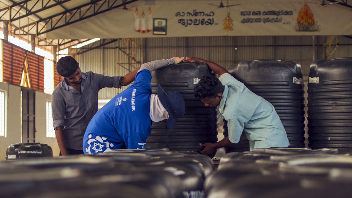 Un voluntario CADENA y un ciudadano Indio ayudan a cargar un tanque de agua en la misión a Kerala.